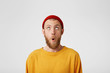© timtimphoto - The bearded guy looks at the top with surprise, mouth rounded. Portrait of a man in a red cap looking at the empty copy space from above, wants to say Wow. That's so unexpected.
