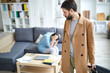 © pressmaster - Young man in beige coat pulling suitcase while leaving for business travel on background of lonely woman