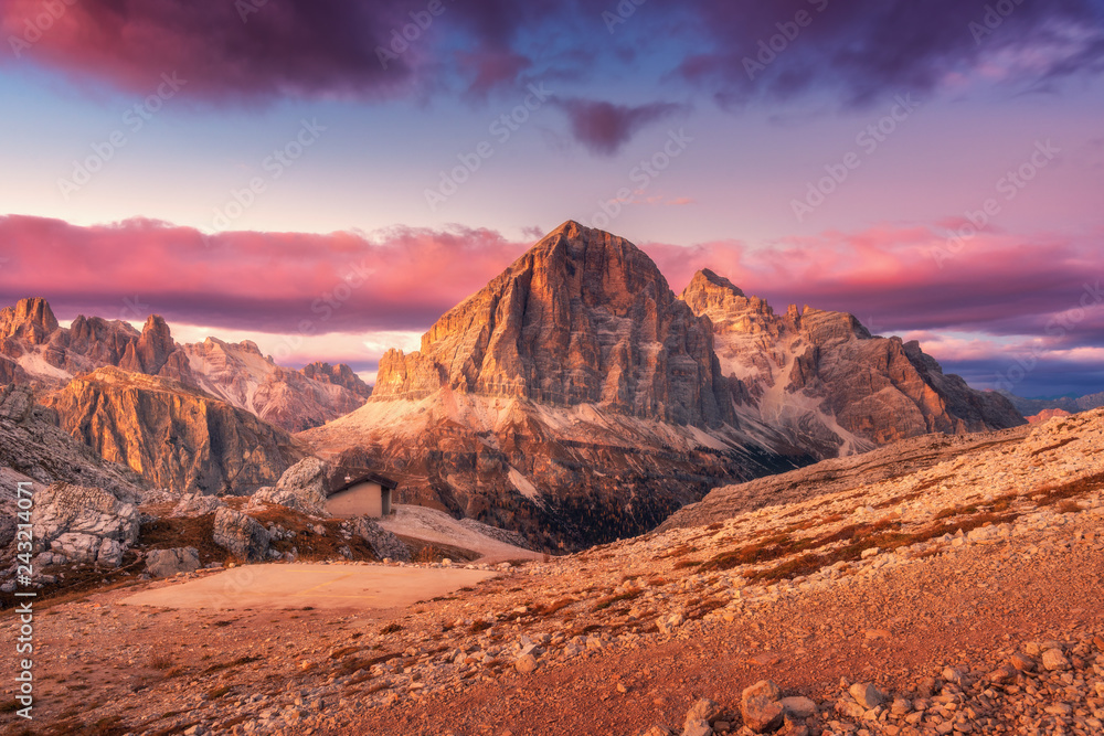 Mountains at sunset in Dolomites, Italy. Landscape with high rocks, stony trail, small house, purple sky with pink clouds in the evening. Autumn scenery with mountain valley. Italian alps at dusk - obrazy, fototapety, plakaty 