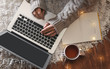 © New Africa - Woman with cup of hot beverage using laptop at home in winter evening, top view