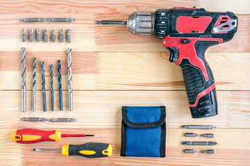 Electric screwdriver with bits and drills on wooden background. Construction tools concept. 