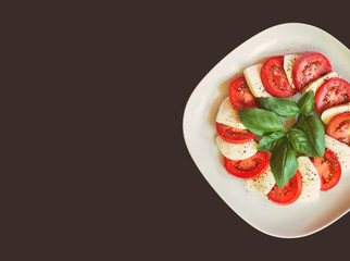 White plate with caprese salad with ripe tomatoes, mozzarella cheese and green basil leaves. Top view, copy space.