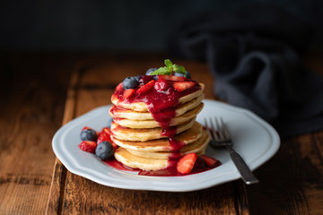 Wall Mural - Tasty Pancakes With Berry Sauce On Wooden Table. Closeup view. Low Key Food Photography