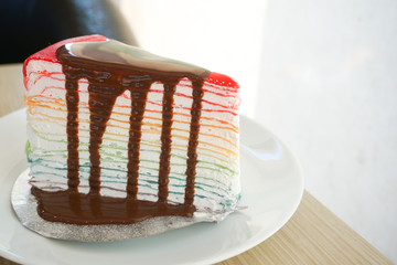 Poster - Rainbow crape cake with chocolate sauce on white plate on wooden table..