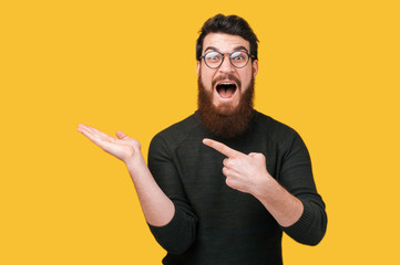 Cheerful bearded hipster man pointing at copyspace over yellow background