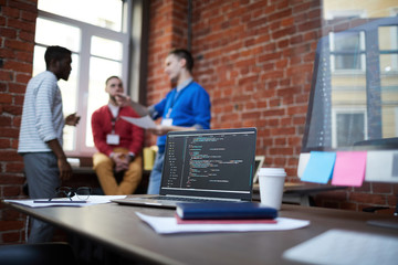technical algorithm or chain of codes on laptop display among other supplies on table and group of c