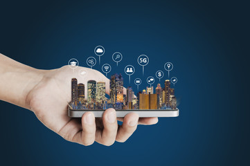 hand holding mobile smart phone with buildings hologram and technology icons. smart city, 5g, intern