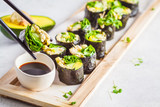 Fototapeta  - Vegan green sushi rolls with avocado, sprouts, cucumber and nori on wooden board, gray background.