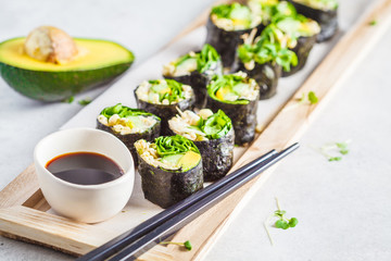 Canvas Print - Vegan green sushi rolls with avocado, sprouts, cucumber and nori on wooden board, gray background.