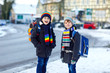 © Irina Schmidt - Two little kids boys of elementary class walking to school during snowfall. Happy children having fun and playing with first snow. Siblings ans friends with backpack in colorful winter clothes.