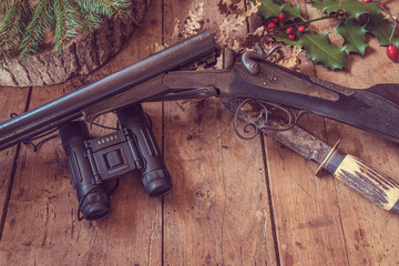 Wall Mural - Beautiful hunting still life: old hunting gun, look-see, knife, dry leaves and berries on old wooden background with copy space