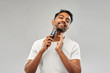 grooming, technology and people concept - smiling indian man shaving beard with trimmer over grey background