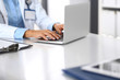 © rogerphoto - Unknown doctor woman typing on laptop computer while sitting at the desk in hospital office. close-up of hands. Physician at work. Medicine and health care concept