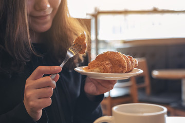 Wall Mural - Closeup image of an asian woman holding and eating a piece of croissant for breakfast in the morning