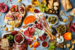 Appetizers table with antipasti snacks and wine in glasses. Brushetta or authentic traditional spanish tapas set, cheese and meat platter over grey concrete background. Top view
