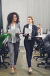 © LIGHTFIELD STUDIOS - smiling young multiethnic businesswomen holding papers and walking in office
