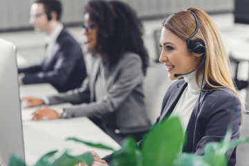 Wall Mural - side view of smiling young businesswoman in headset working with colleagues in call center