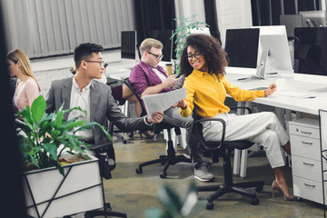 Wall Mural - smiling young multiracial business people holding papers and working together in office