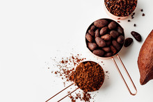 Rose Gold Measuring Cups Of Cocoa Beans, Cacao Nips, Cocoa Powder And Cocoa Pods On A White Background, Flat Lay Healthy Food Concept