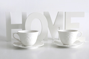 White letters, word home and two elegant cups on white background. Home decor