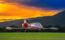Airplane Model Of Bombardier Learjet 35A Parking On The Apron With Beautiful Sunset And Mountain Background.
