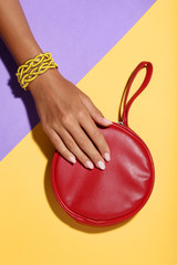 Poster - Female hand with bracelets and red handbag on colorful background