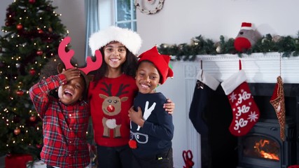 Wall Mural - Portrait Of Children Wearing Festive Jumpers And Hats Celebrating Christmas At Home Together