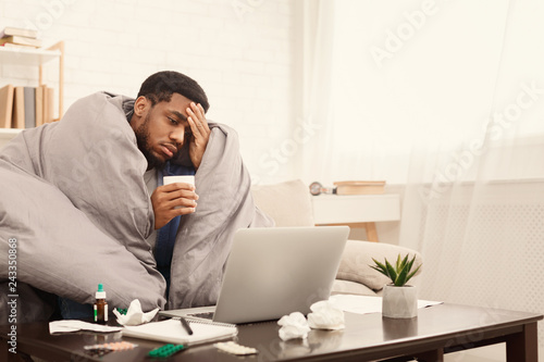 Sick african-american man working on laptop at home Poster Mural XXL