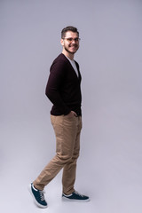 Wall Mural - Full length portrait of a smiling young man walking isolated over gray background.