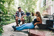 © Manu Reyes - Smiling young couple sitting in the garden chairs near their wooden house with their smart phone