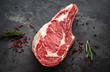 raw cowboy steak with seasonings on stone background, prime rib eye on bone, top view