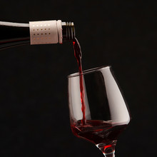 Close-up Of Red Wine Pouring In Glass Against Black Background