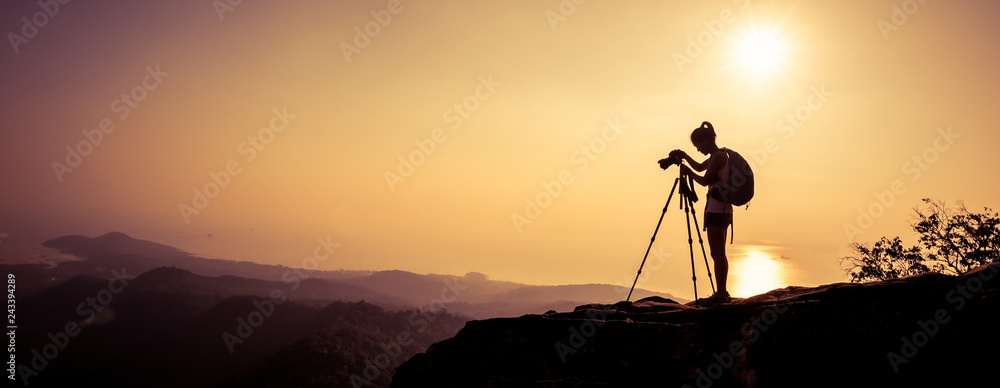 woman photographer taking photo on sunset mountain peak - obrazy, fototapety, plakaty 