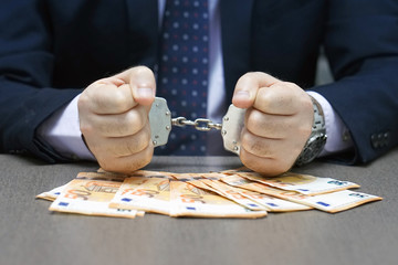 Businessman in office in handcuffs holding a bribe of euro banknote. Arrested terrorist. Financial crime, dirty money and corruption concept. Selective focus.