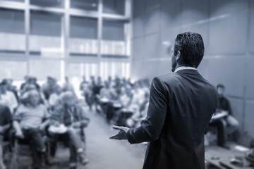 Wall Mural - Rear view of speaker giving a talk at business meeting. Audience in the conference hall. Business and Entrepreneurship concept. Black and white blue toned image.