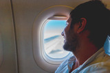 Fototapeta  - handsome man passenger traveler looking at window in airplane, travel by flight, man tourist sitting in air plane watching outside 