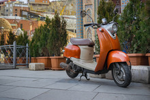 Old Vintage Orange Scooter Parked In Trees, Greens And Bushes On Pavement In Old City Of Tbilisi, Georgia. 