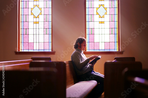 Cuadros en Lienzo Christian Man Sitting Alone in Dark Empty Church Pew by Bright Stained Glass Win