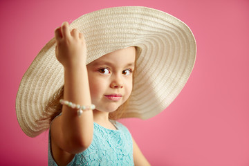 Wall Mural - Beautiful little girl in beach hat stands over pink isolated background.