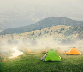 Wall Mural - green and orange tents on plain in mountains on foggy morning
