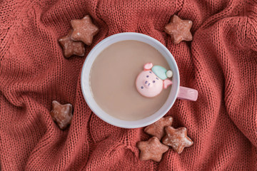 Wall Mural - Cup of coffee with milk, marshmallow pig and star shaped ginger cookies on warm knitted coral blanket.