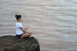 Girl meditates sitting on a stone cliff not looking at the camera