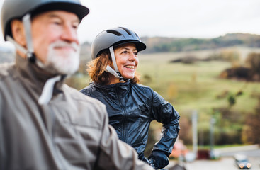 active senior couple with electrobikes standing outdoors on a road in nature.