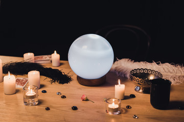 selective focus of crystal ball near candles and feathers on wooden table isolated on black