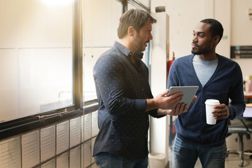 colleagues standing together in modern office going over ideas on tablet