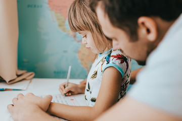 Wall Mural - Father helps his little daughter to write at the desk in the room with the map on the wall