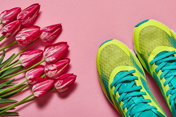 Pair of sport shoes and tulips on pink pastel background. New sneakers, copy space. Overhead shot of running foot wear. Top view, flat lay. Spring, sport, minimal concept
