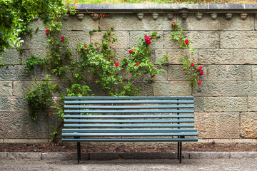 Empty blue wooden bench stands near stone wall