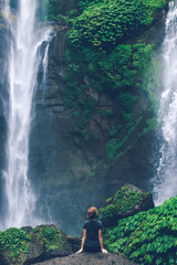 Young woman posing on a great Sekumpul waterfall in the deep rainforest of Bali island, Indonesia.