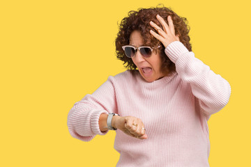 Wall Mural - Beautiful middle ager senior woman wearing pink sweater and sunglasses over isolated background Looking at the watch time worried, afraid of getting late